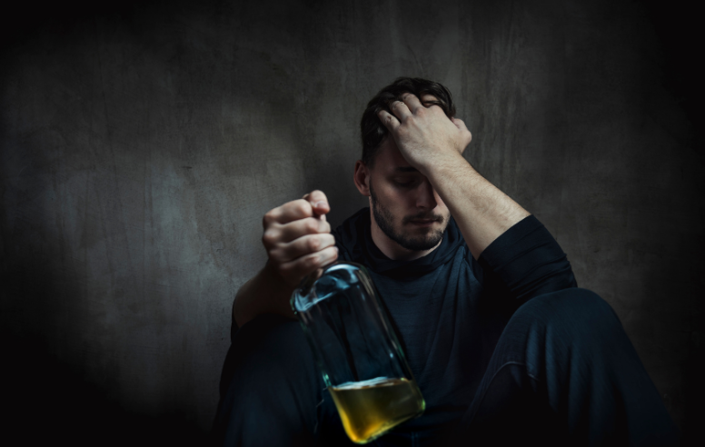 Man sitting on the floor with a bottle of alcohol in his hands.